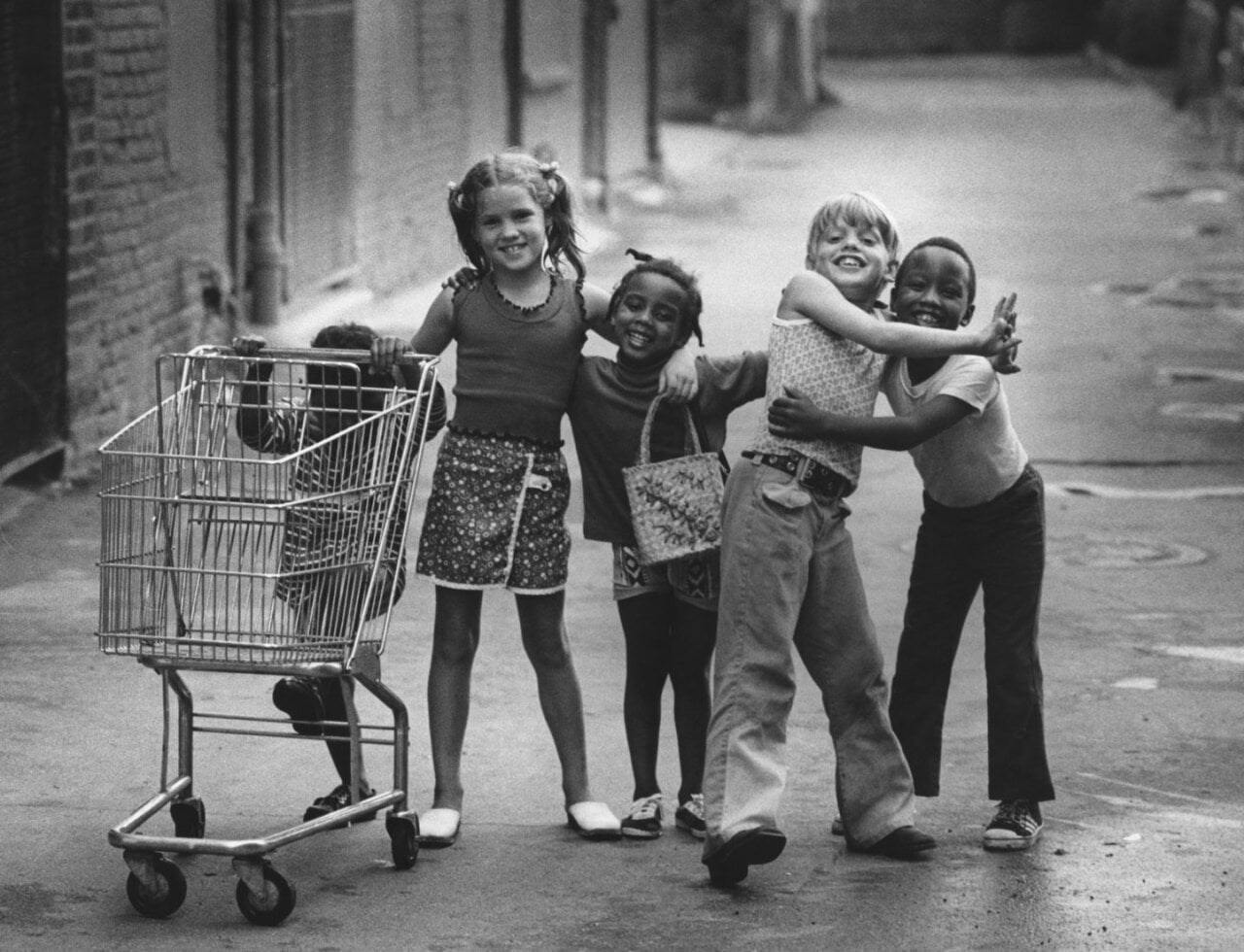A group of kids with their arms around each other, standing with a shopping trolley on a street in downtown Mount Clemens, Michigan