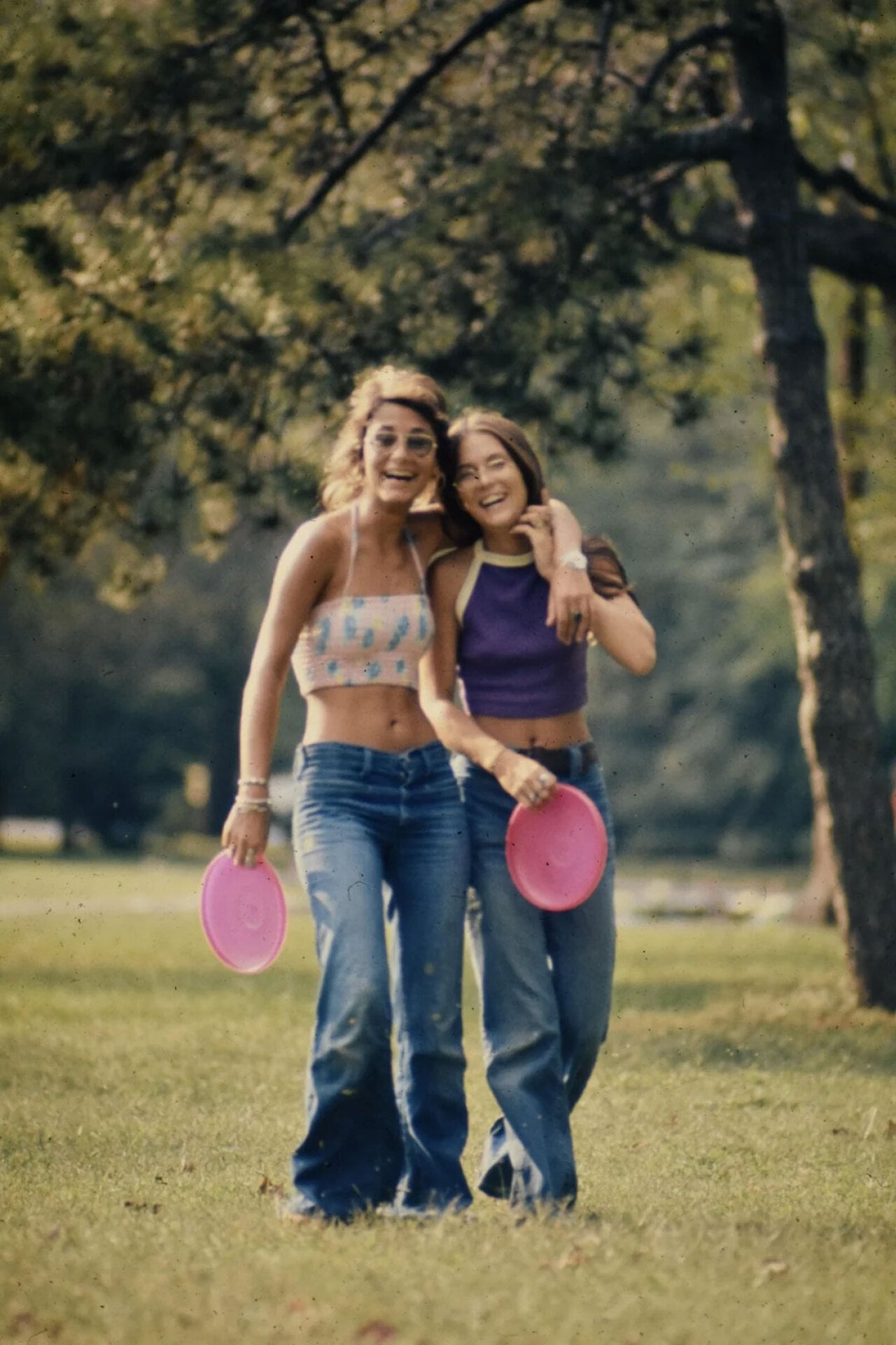 Two young woman holding pink frisbess, laughing