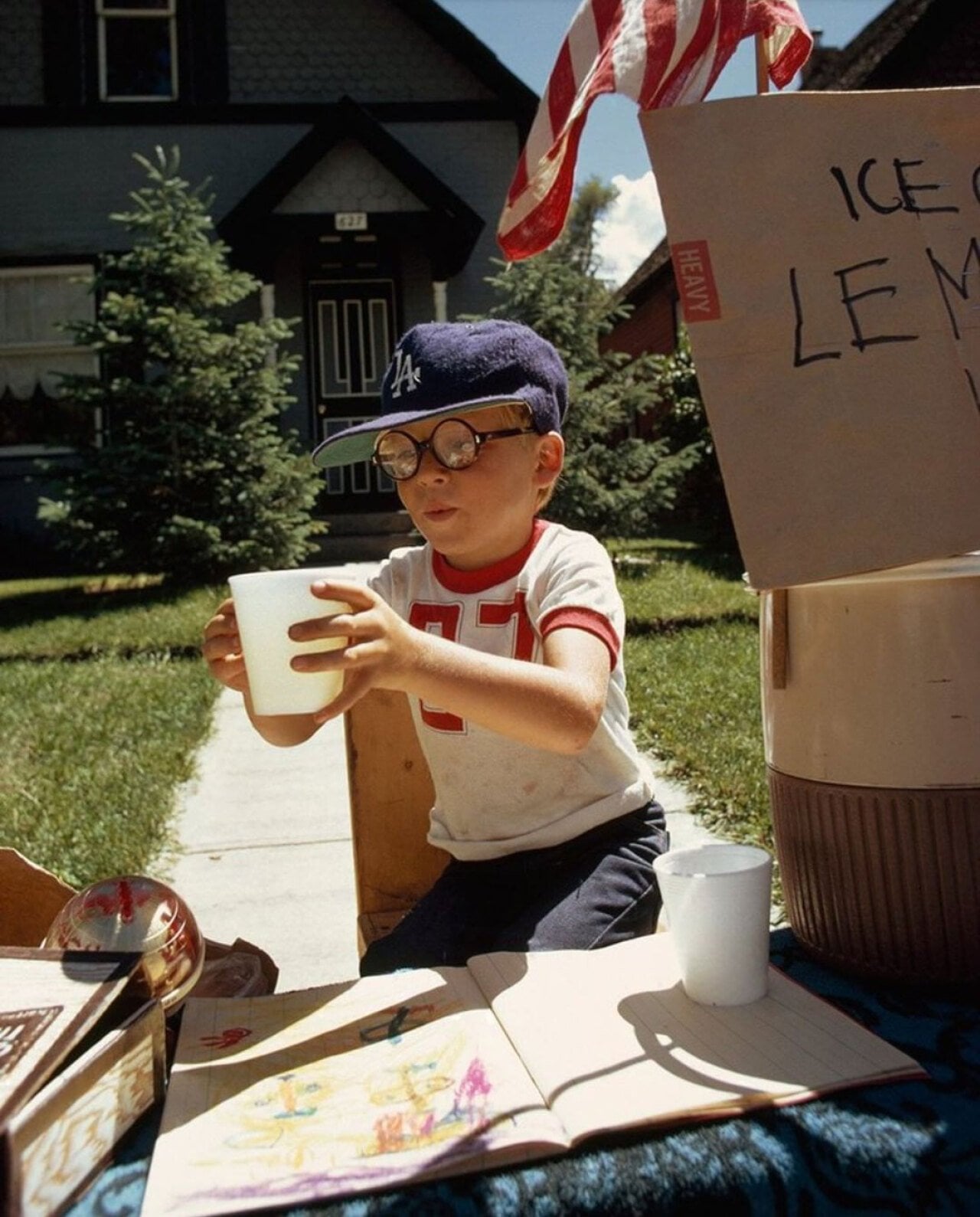 A boy wearing a Dodgers ball cap selling lemonade in his front yard