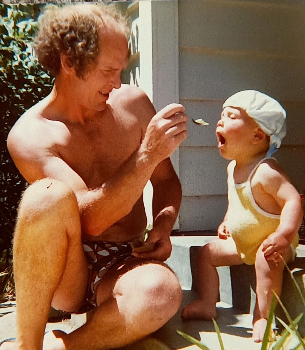 A father feeding his son on the porch on a sunny day.