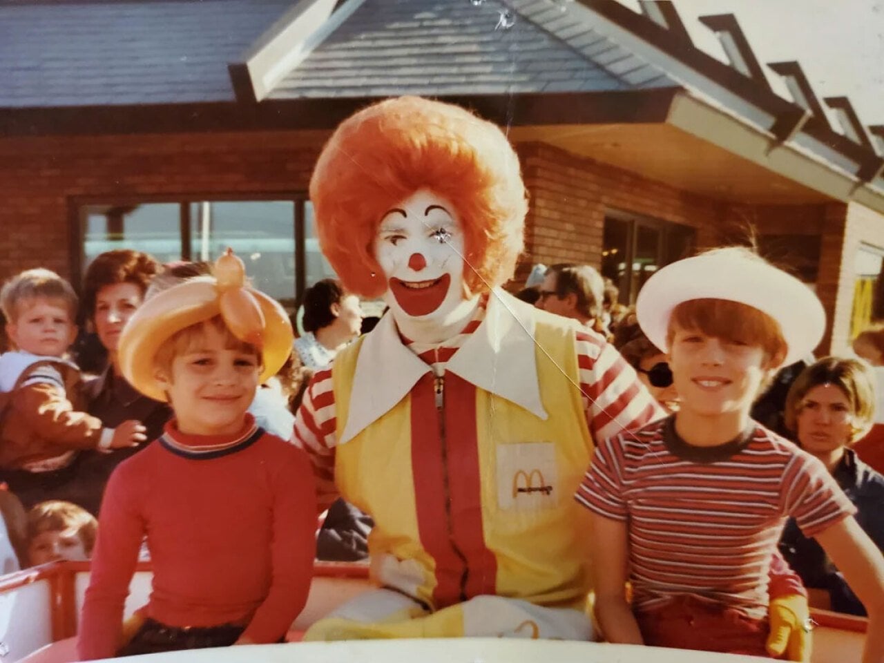 Two boys sitting on either side of a man dressed as Ronald McDonald