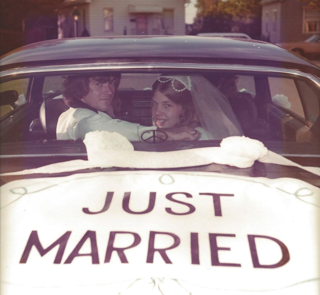 A couple inside a car looking through the back window at the camera. Just Married is painted on the trunk.