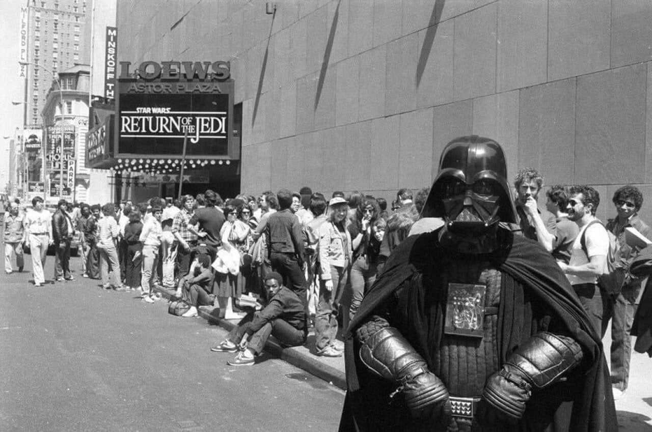 Man dressed up as Darth Vader in front of a long line of people waiting to see Return of the Jedi