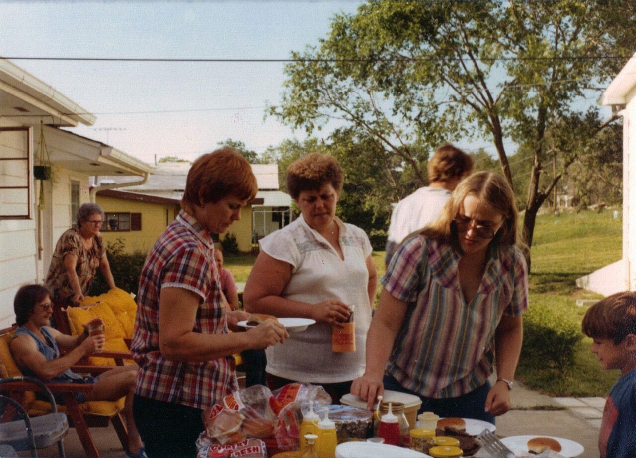 A family hanging out in a backyard, preparing some hamburgers