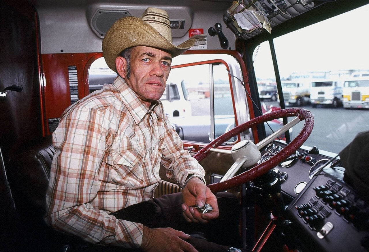 Photograph of a man in a cowboy hat sitting behind the wheel of a big rig
