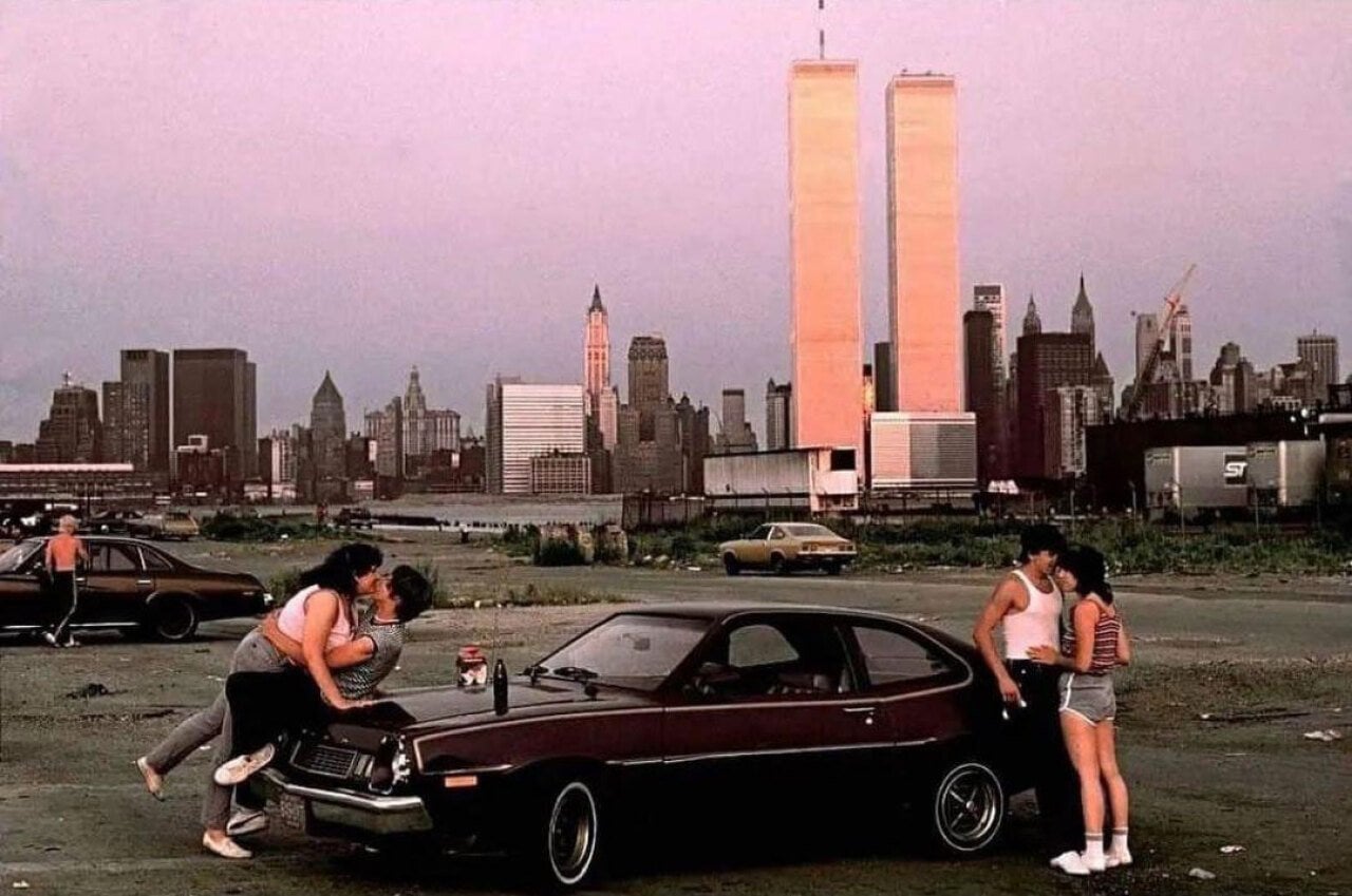 Couples hanging out on a car in New Jersey with Manhattan behind them