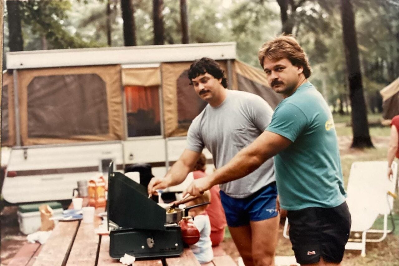 Two very muscular men cooking while camping