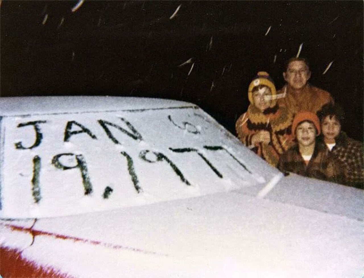 Color photo of a family posing behind a snow-covered car hood at night in Miami, Florida. The date 