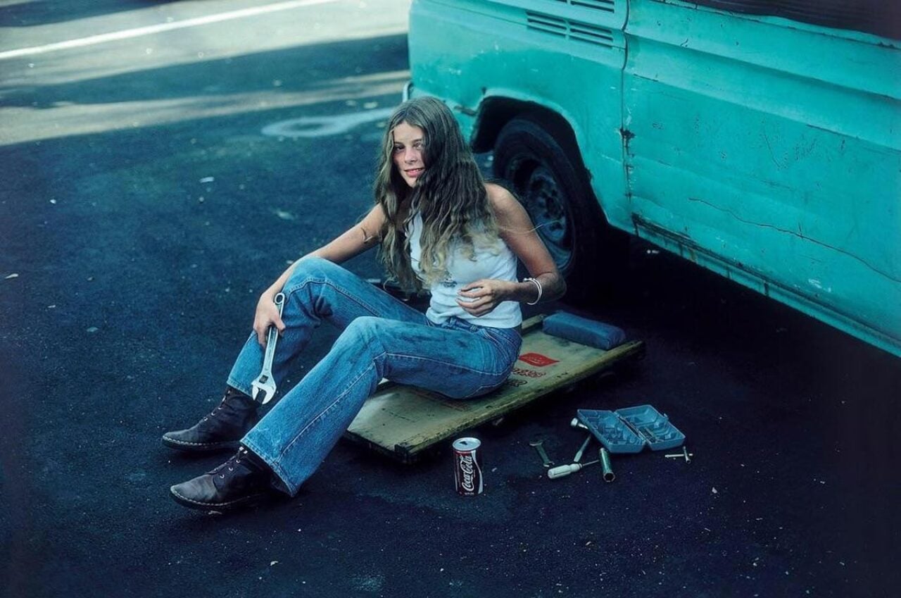 A woman in jeans and boots working on her blue VW van