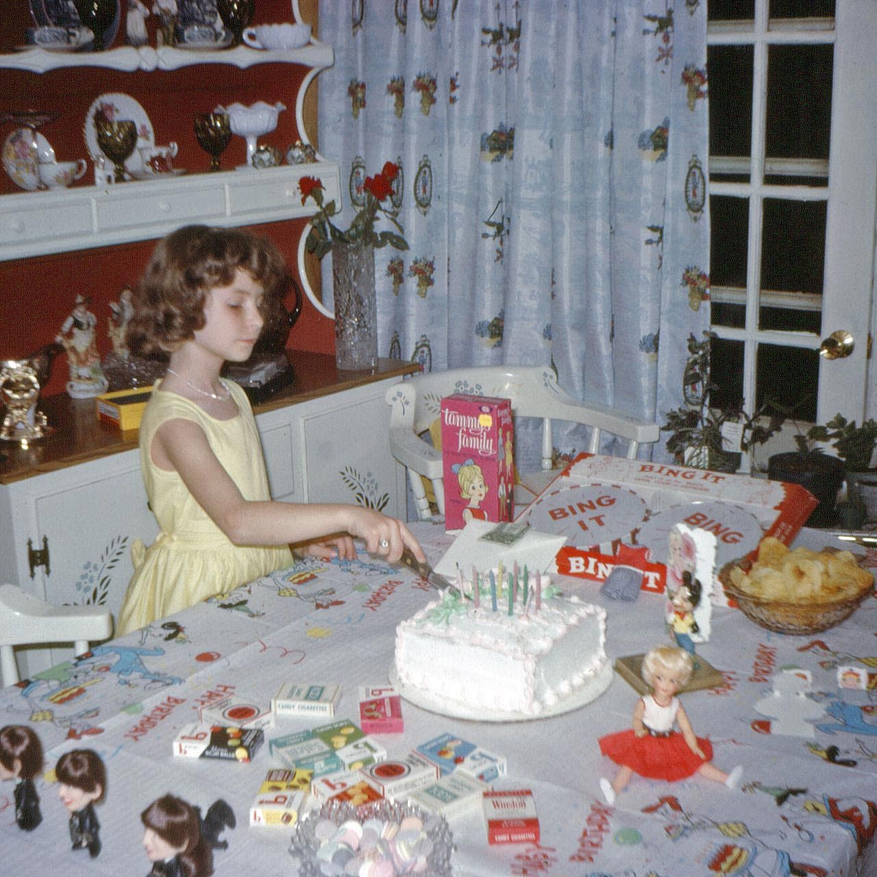 A little girl in a yellow dress cutting into her birthday cake.