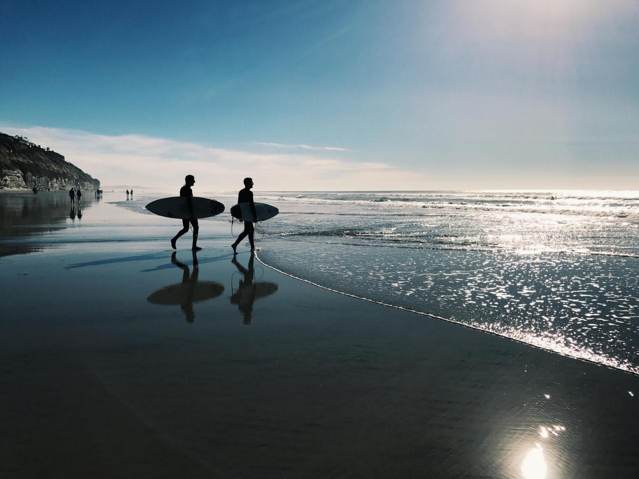 People walking with surfboards on beach.