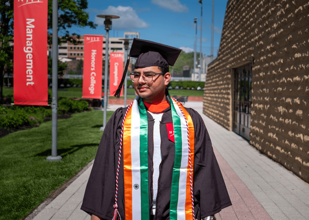 Graduate standing on the campus of NJIT in cap and gown.