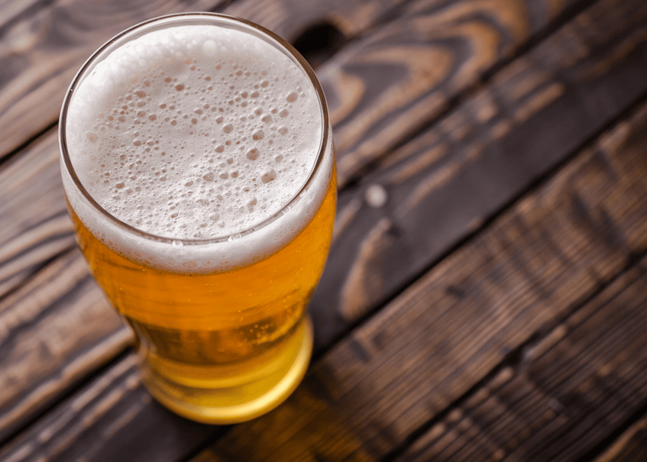 A pint glass filled with beer sits on a wood counter.