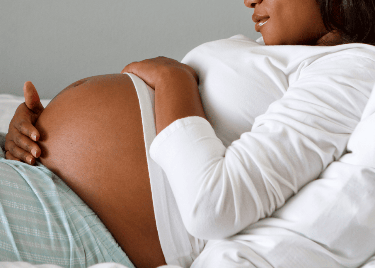 A pregnant person lying in a hospital bed cradling her stomach.