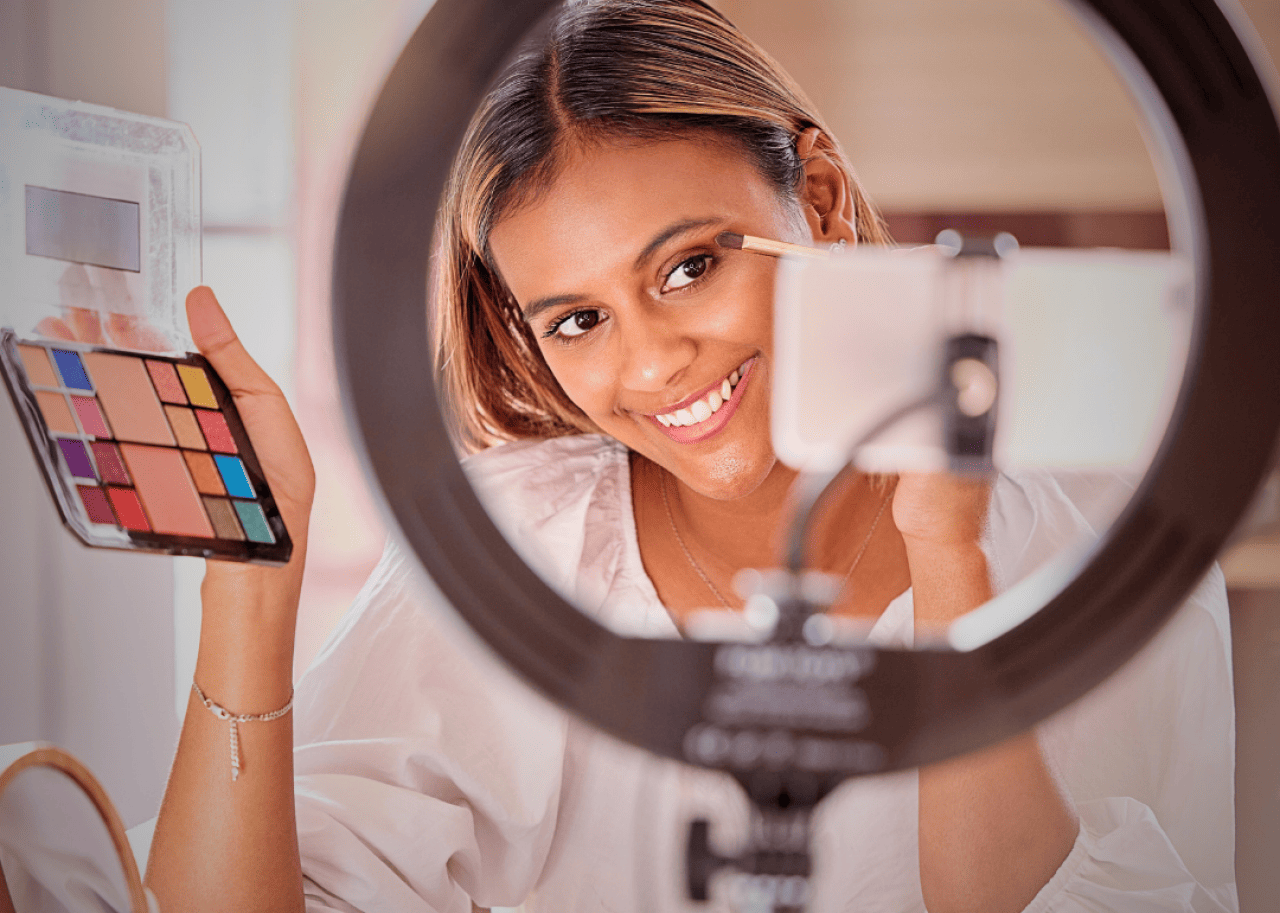 A young woman applying eye makeup looking at the phone in front of her. 