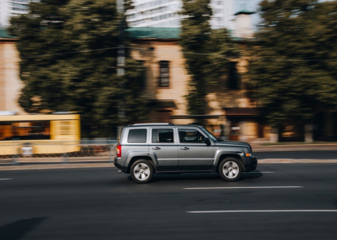 A gray Jeep Patriot speeding down a highway.