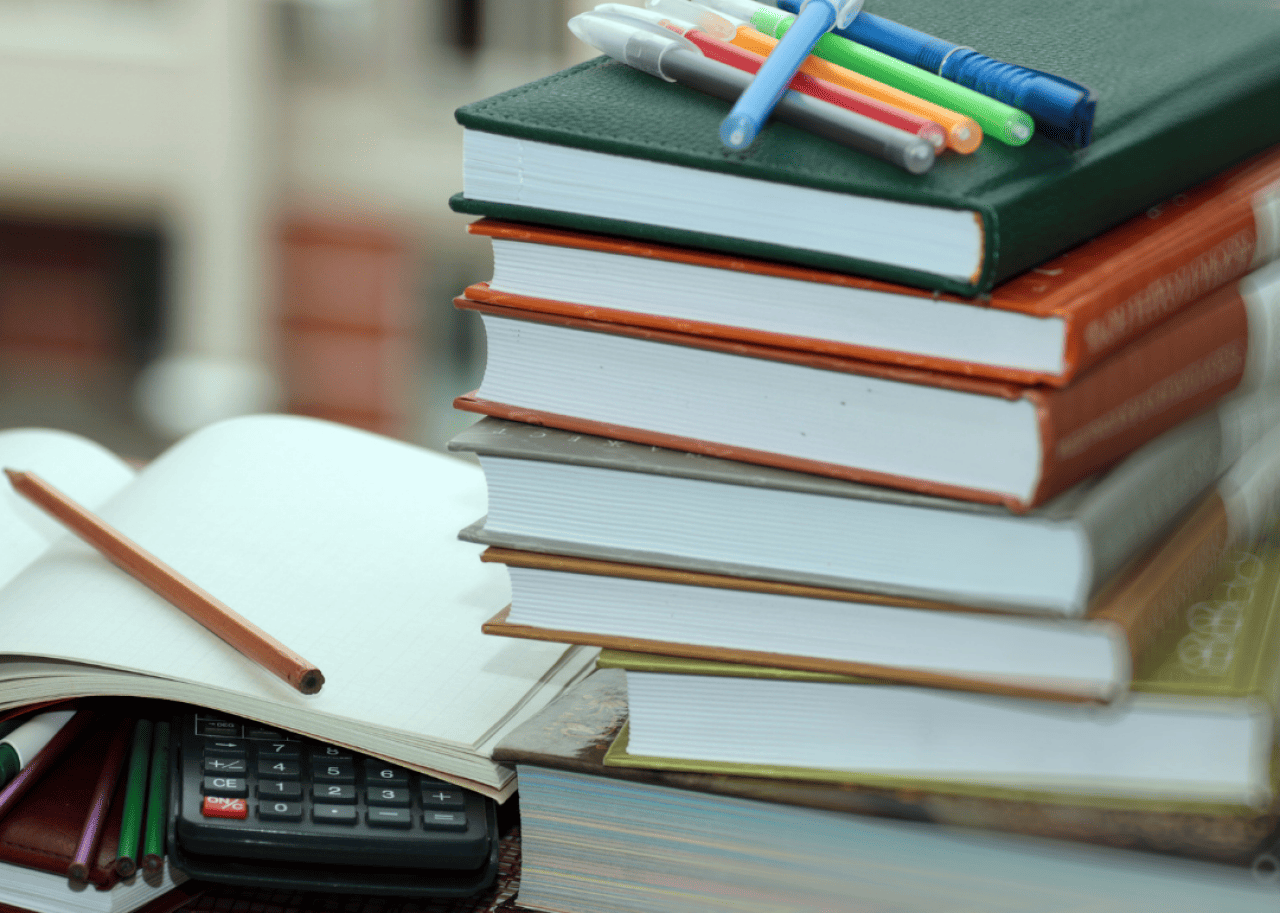A stack of textbooks with pens on top of them next to an open notebook.