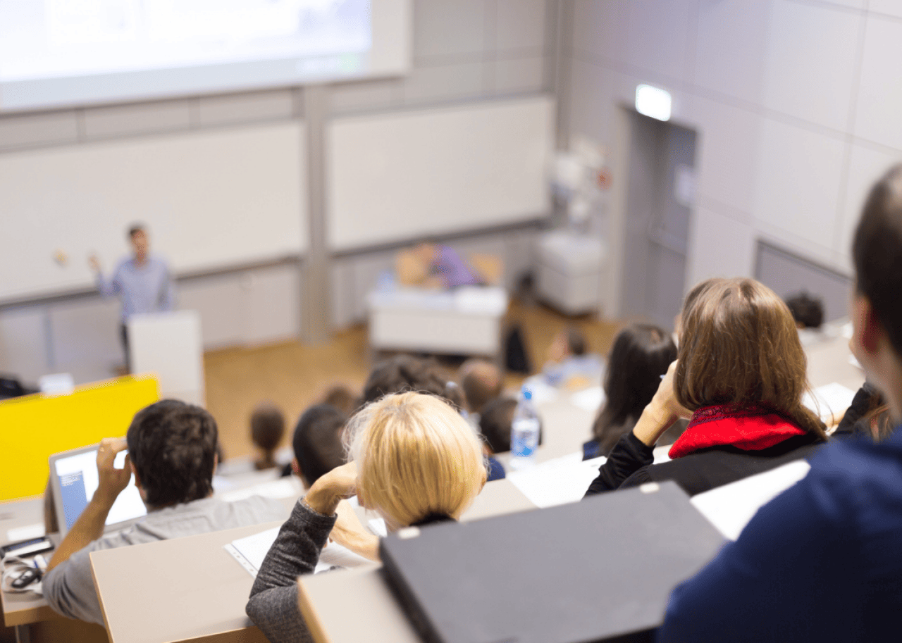 Students listening to their professor speak in a large lecture hall.