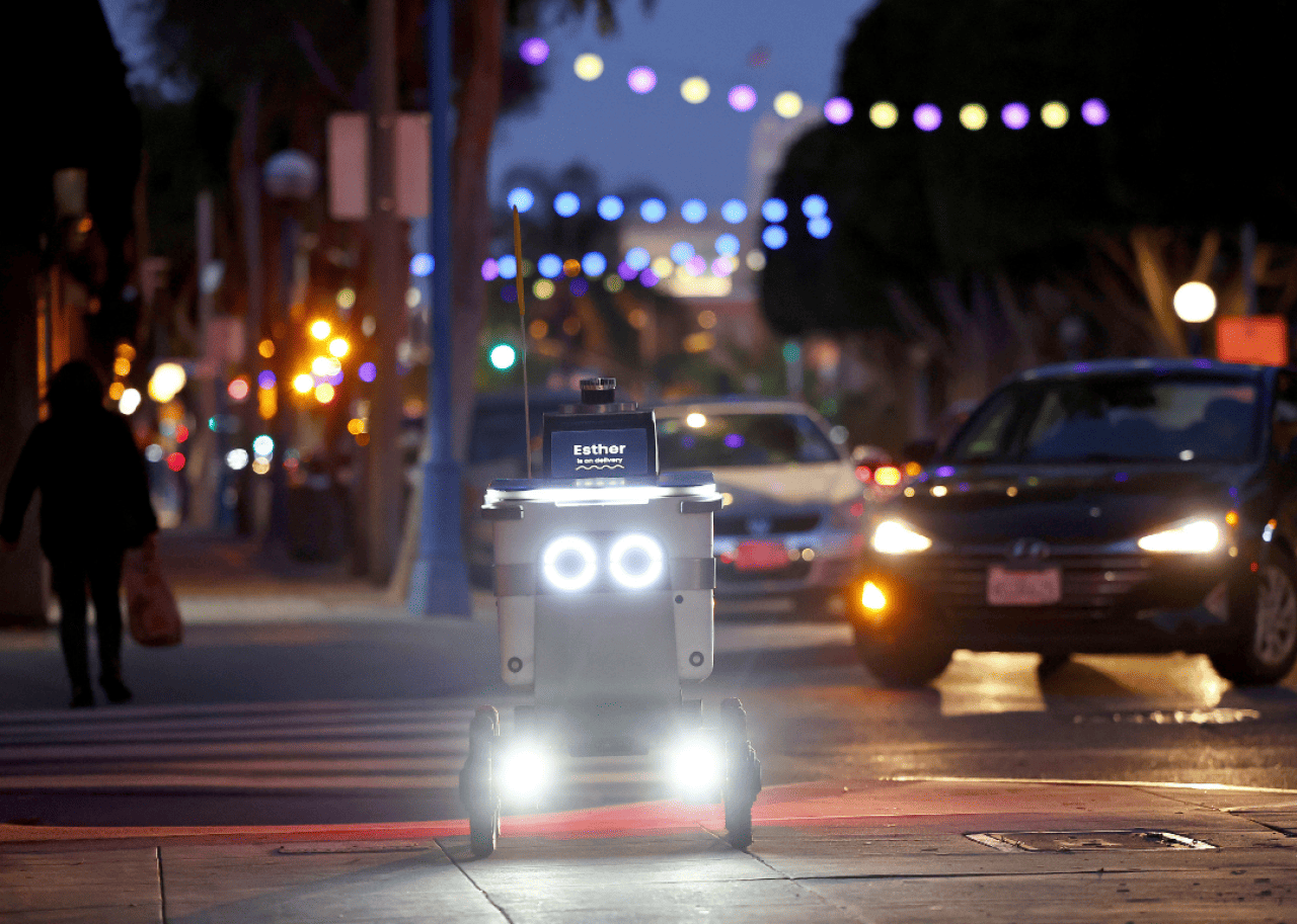 An autonomous robot with the name Esther displayed on its screen making a delivery in the city.