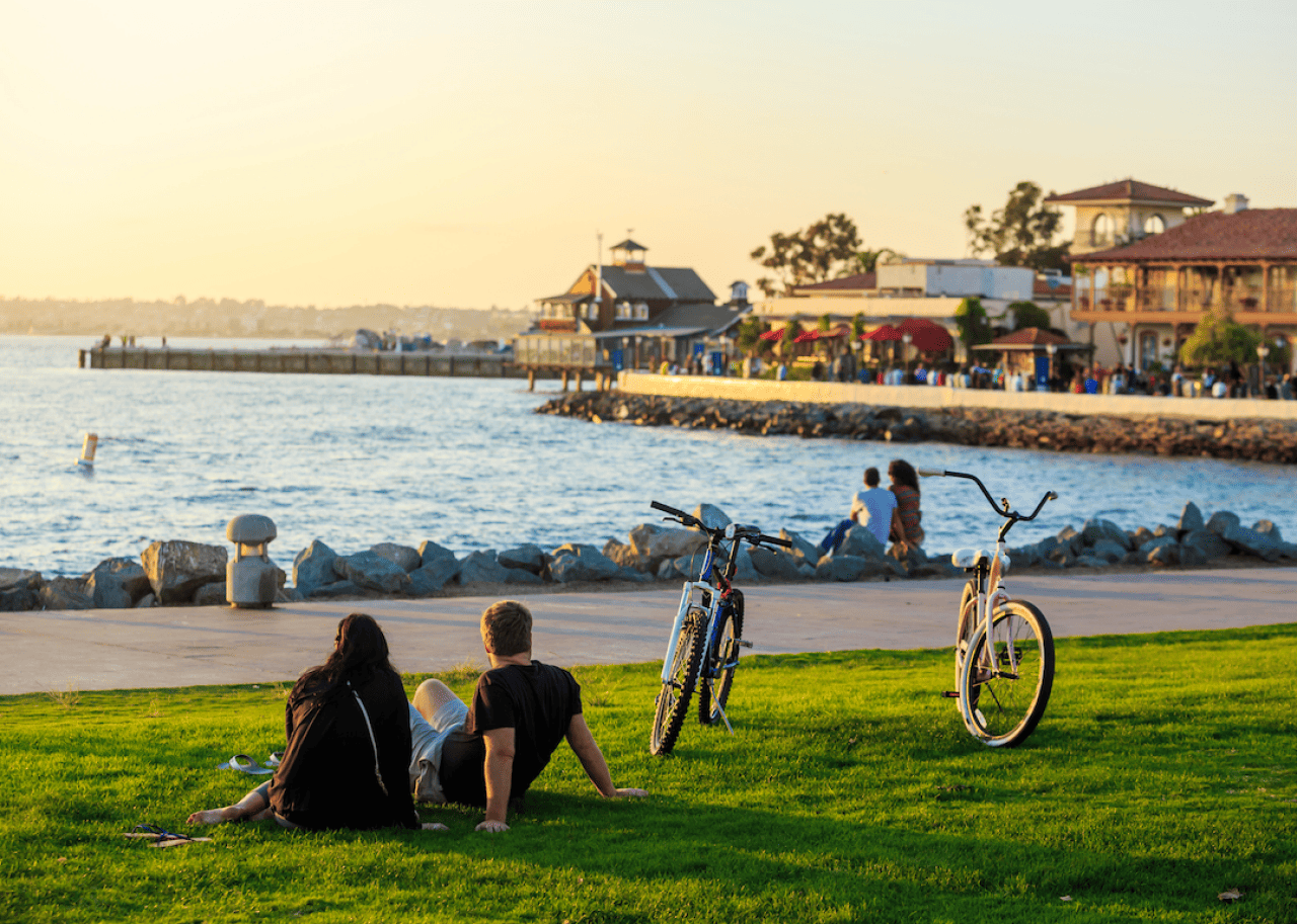 People sitting in the grass by the water with bicycles parked on the side.