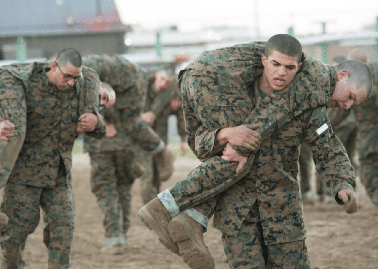 Men in camo carrying other men on their backs.