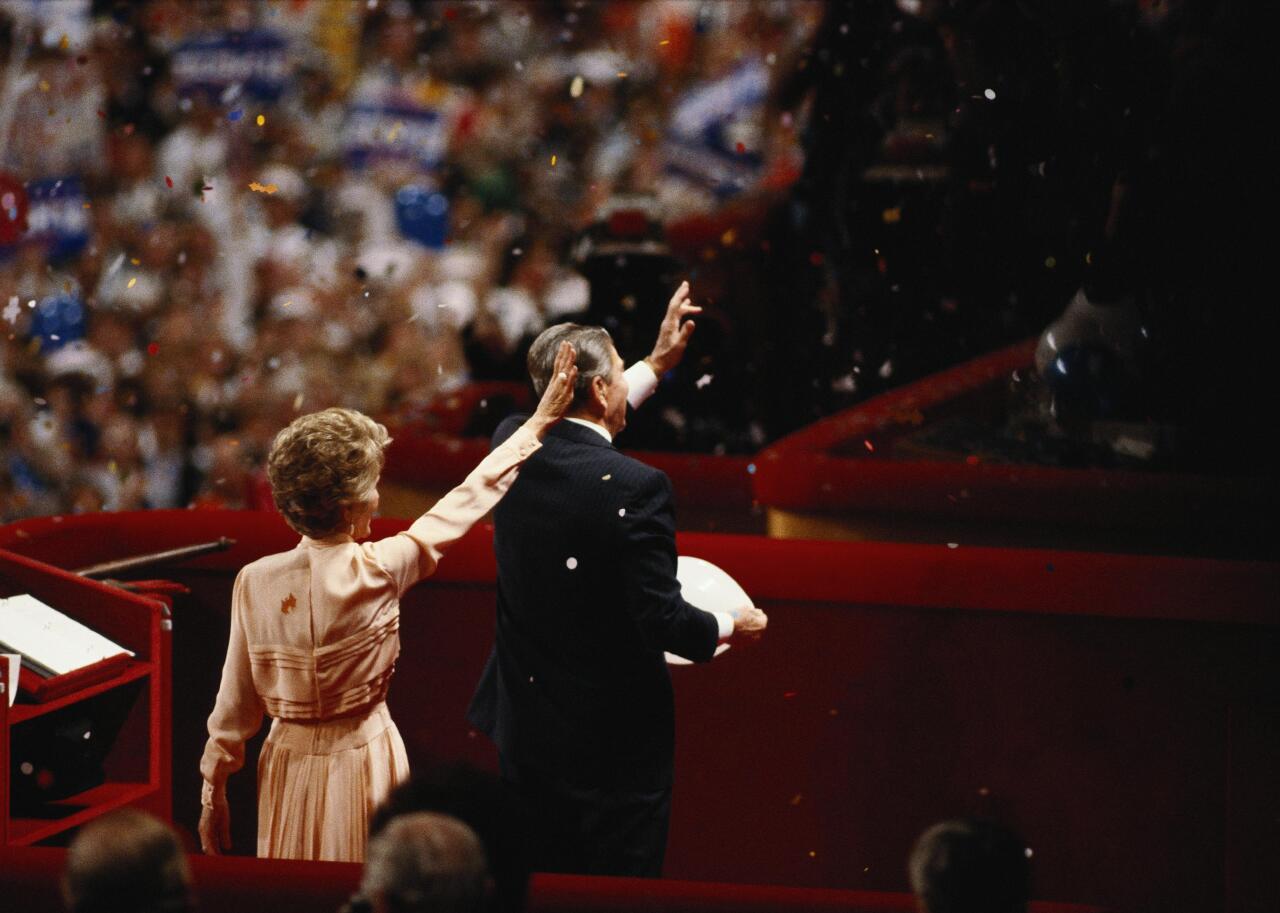 President Ronald Reagan and First Lady Nancy Reagan waving to crowd as confetti falls on them.