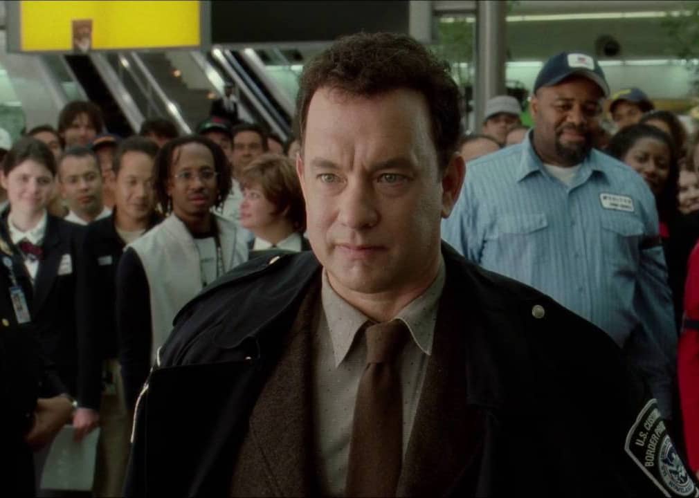 A customs officer stands with a crowd of people behind him.