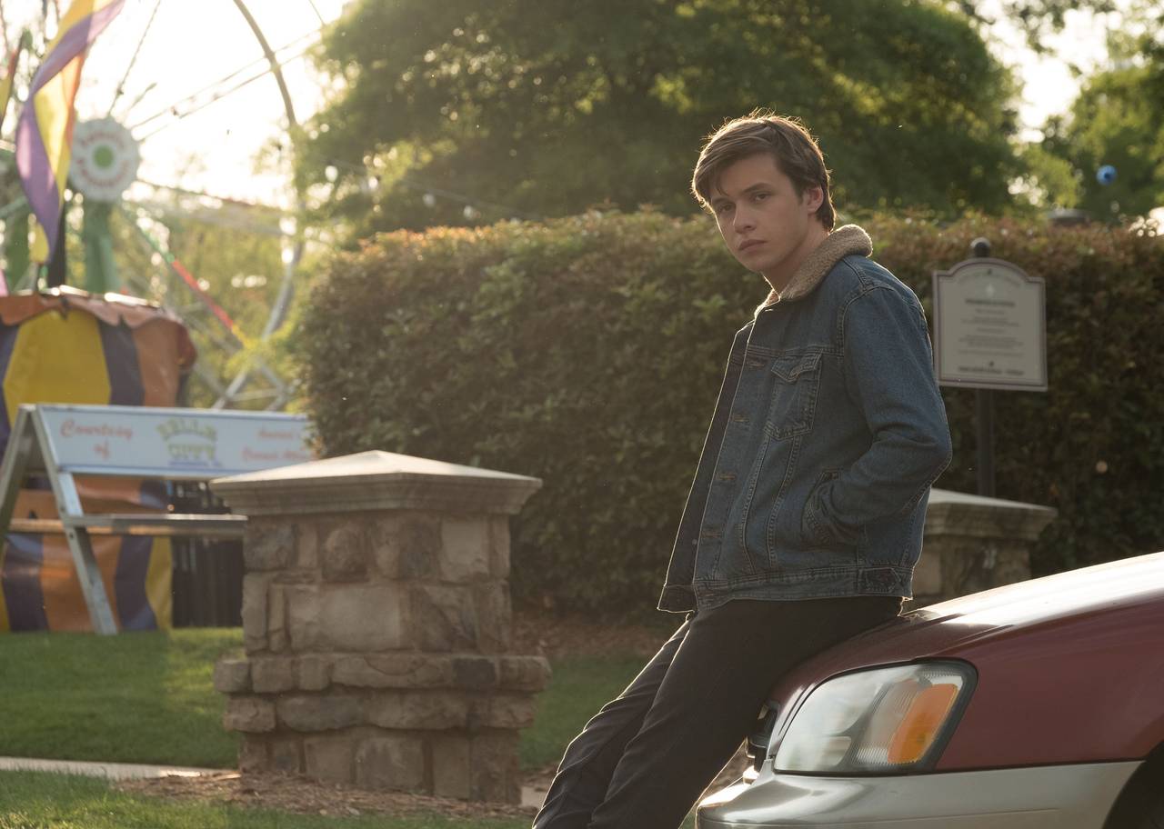 A young man sits on the hood of a car.