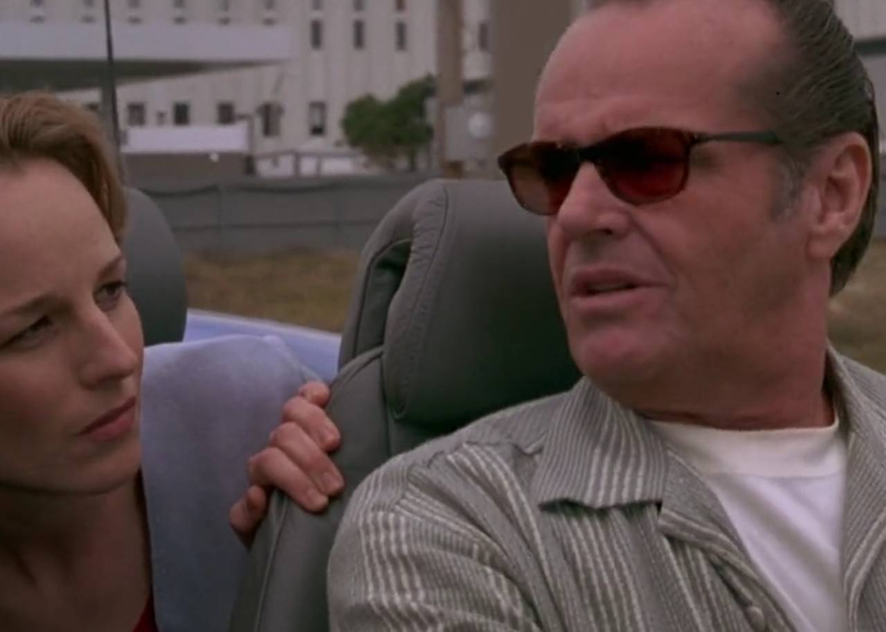 A woman in the backseat of a convertible car leans up to talk to the driver.