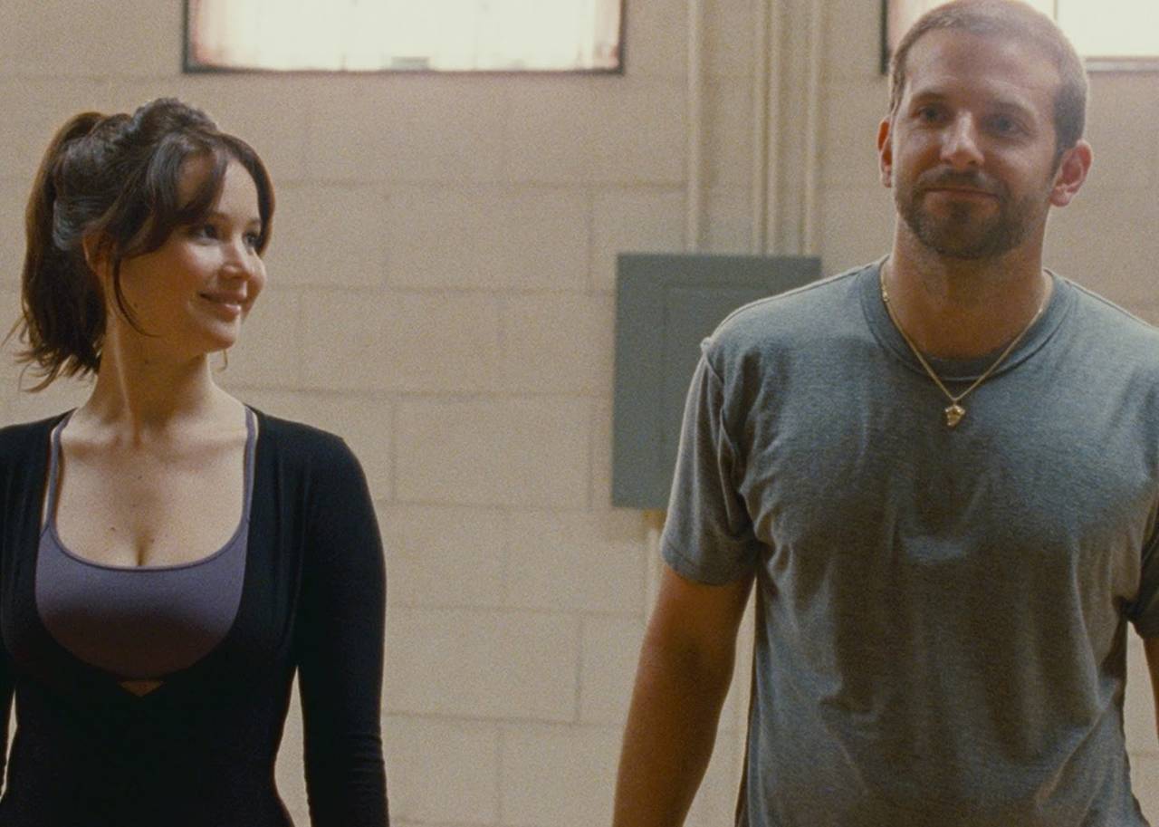 A young man and woman in workout clothes stand ready to dance and smile.
