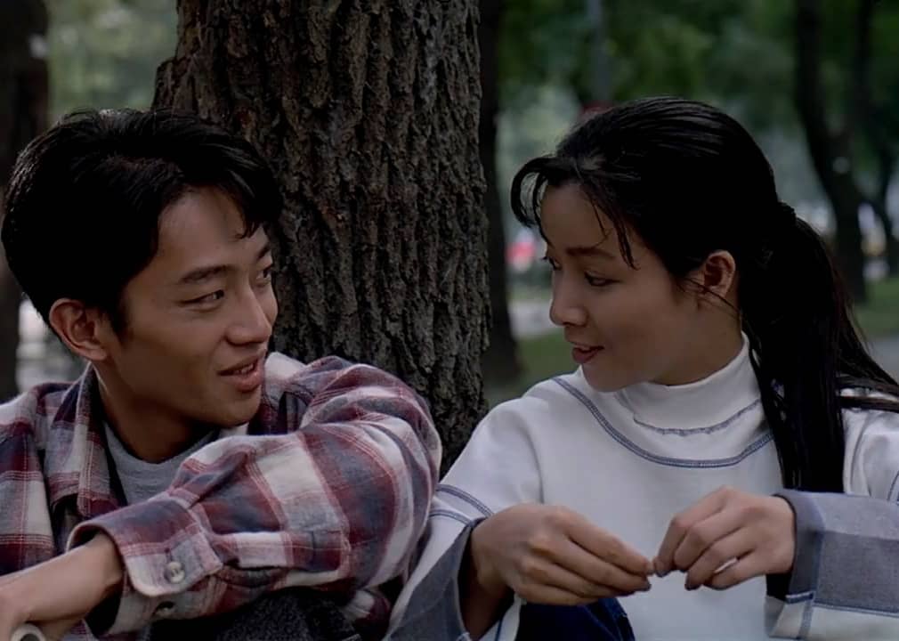 A boy and a girl sit next to a tree staring at each other.