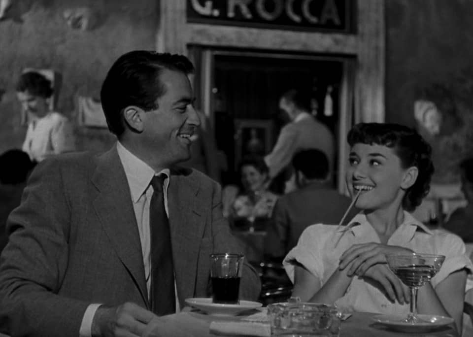Man and woman sit having drinks and laughs.