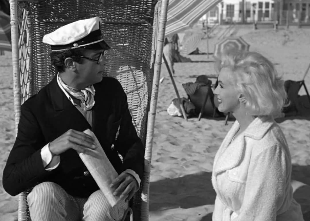 A man and woman on the beach, she in a robe and he in a suit.