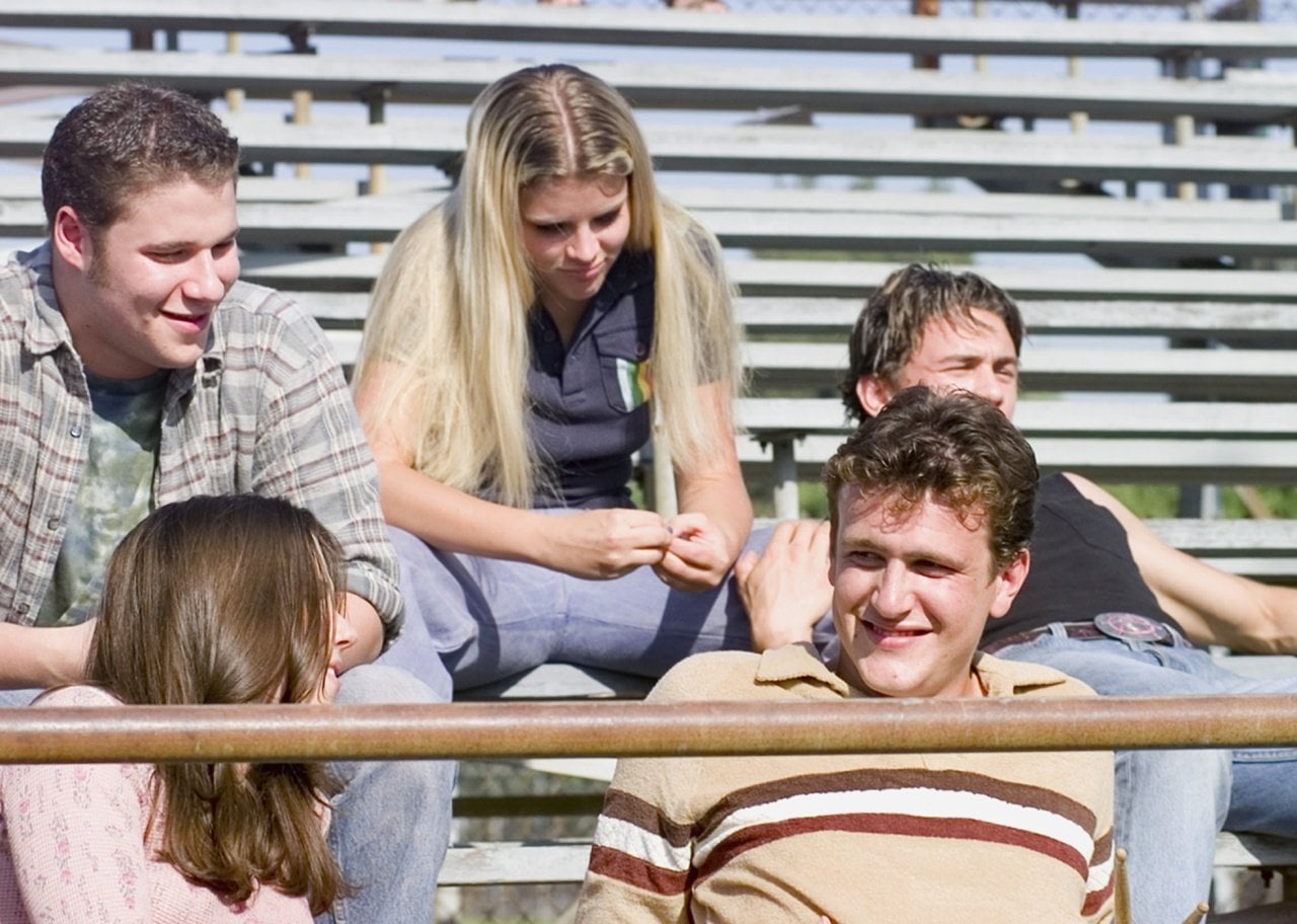 Linda Cardellini, James Franco, Jason Segal, Seth Rogan and Busy Philipps sitting on the bleachers outside.