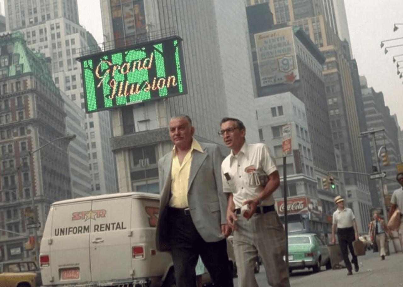 A scene from the film Koyaanisqatsi, with two middle-aged men walking down a busy New York City street. 