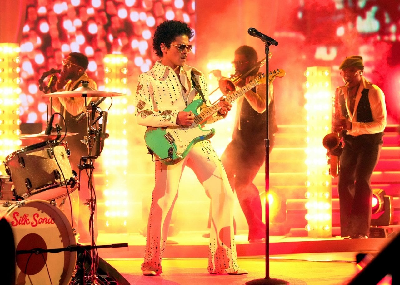 Bruo Mars and his band perform onstage engulfed in golden light.