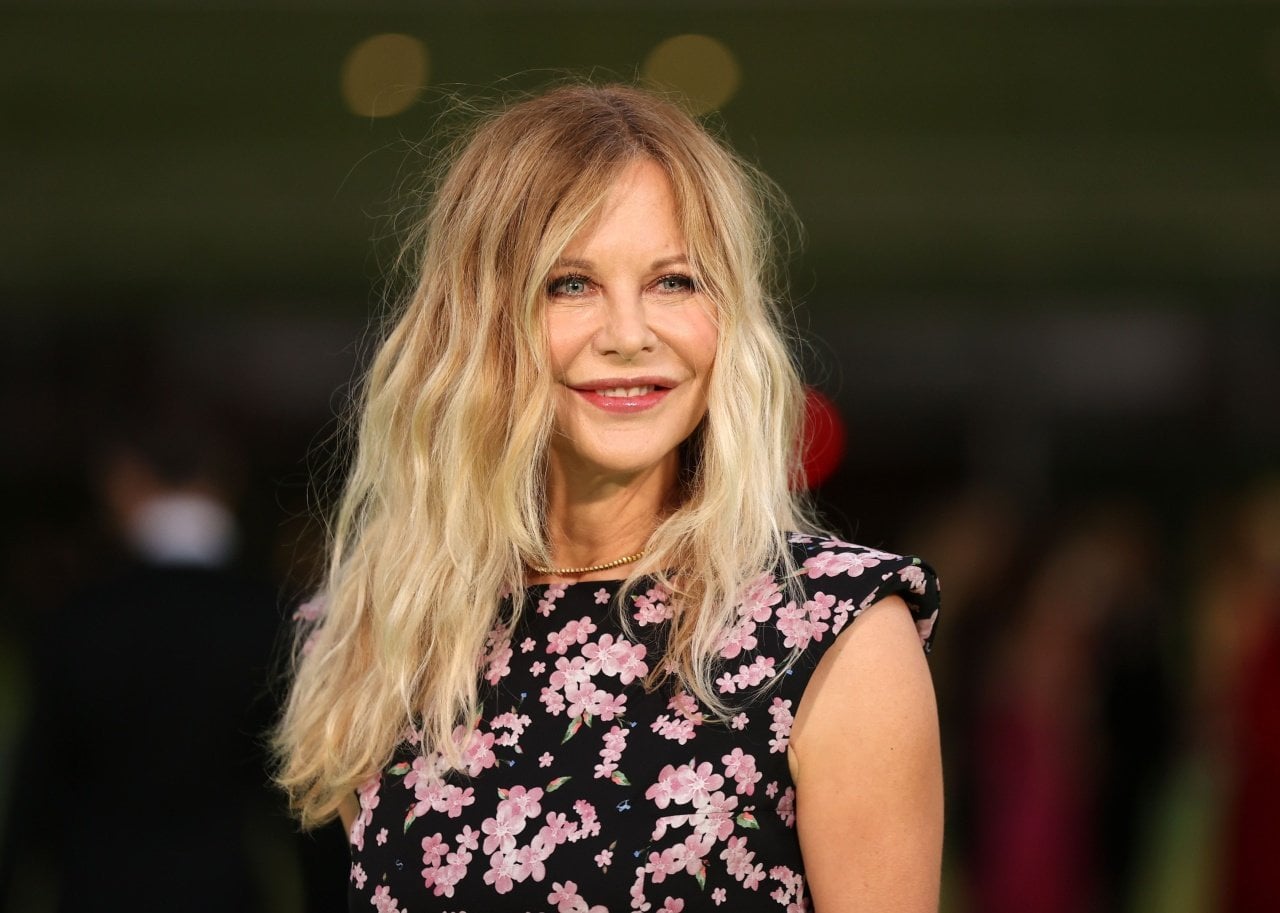 Meg Ryan smiling in a black and pink floral cap sleeved dress.