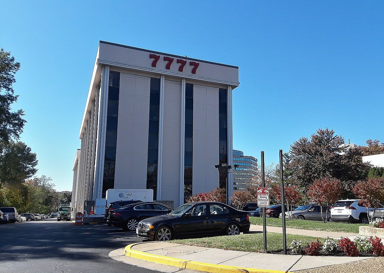 A tall White Stratford University building and parking lot.