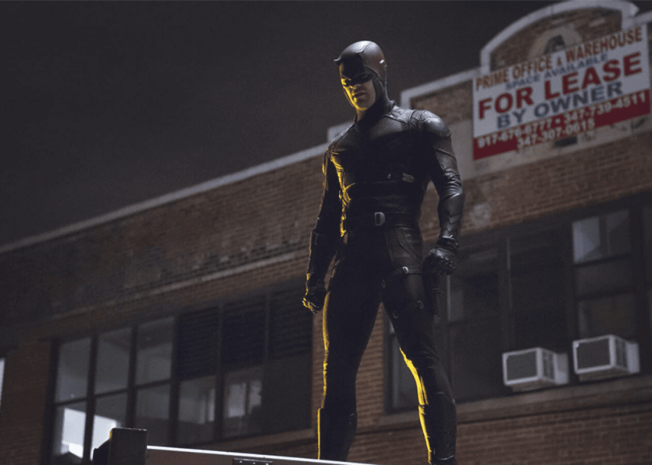 A man stands on a rooftop wearing a dark red tight suit from head to toe.