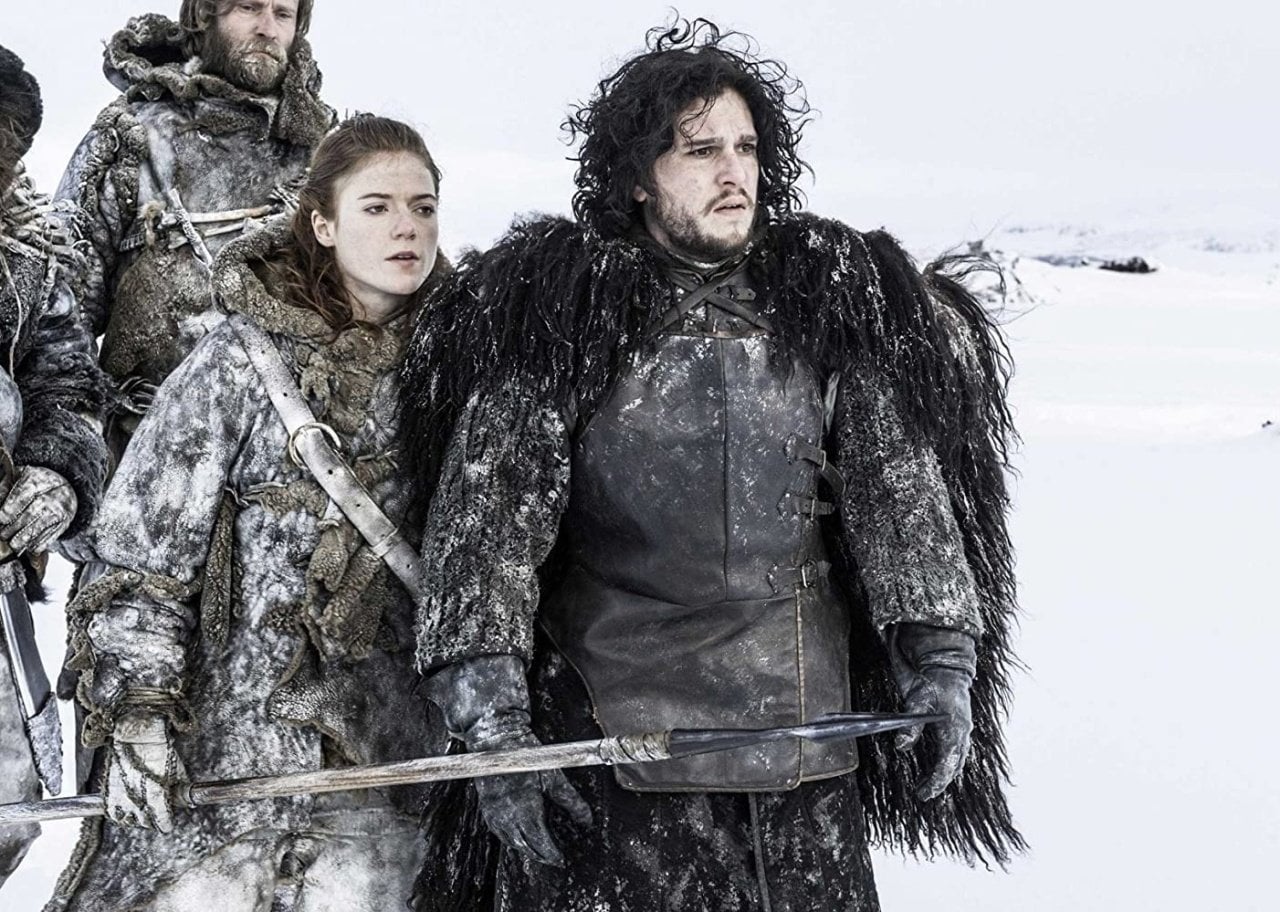 Kit Harington and a group of people stand in the deep snow wearing fur and thick winter clothing.