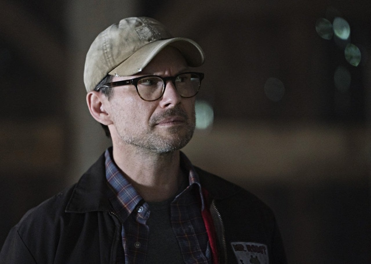 Christian Slater in a brown ball cap looking skeptical.