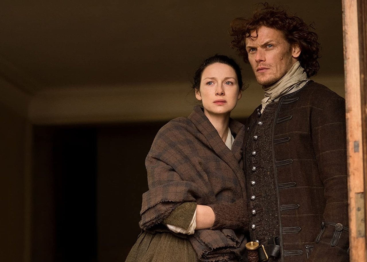 A man and a woman stand holding onto each other in a doorway looking out.