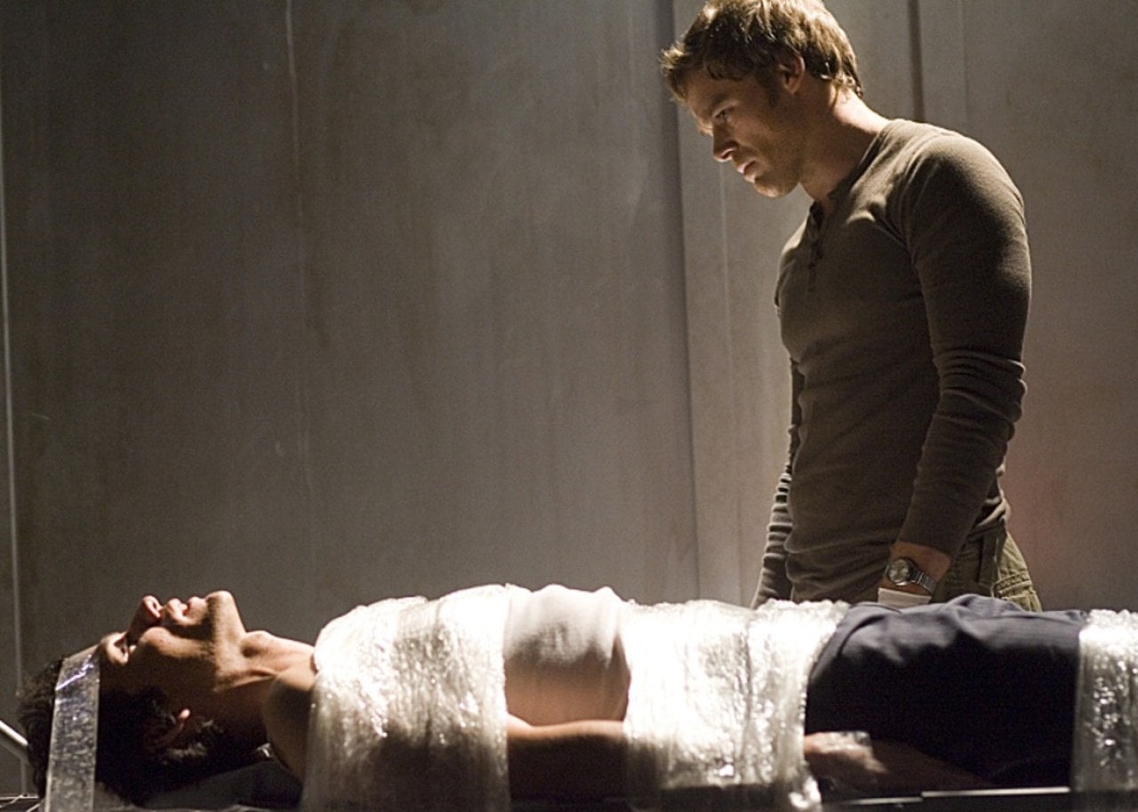Michael C. Hall stands over a person tied to a table.