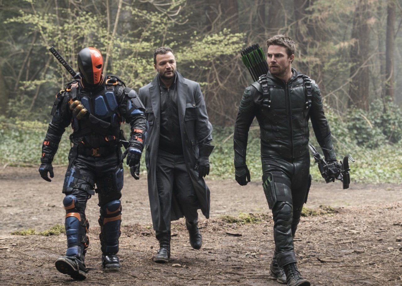 Three men in all black gear and arrows walk through the forest.