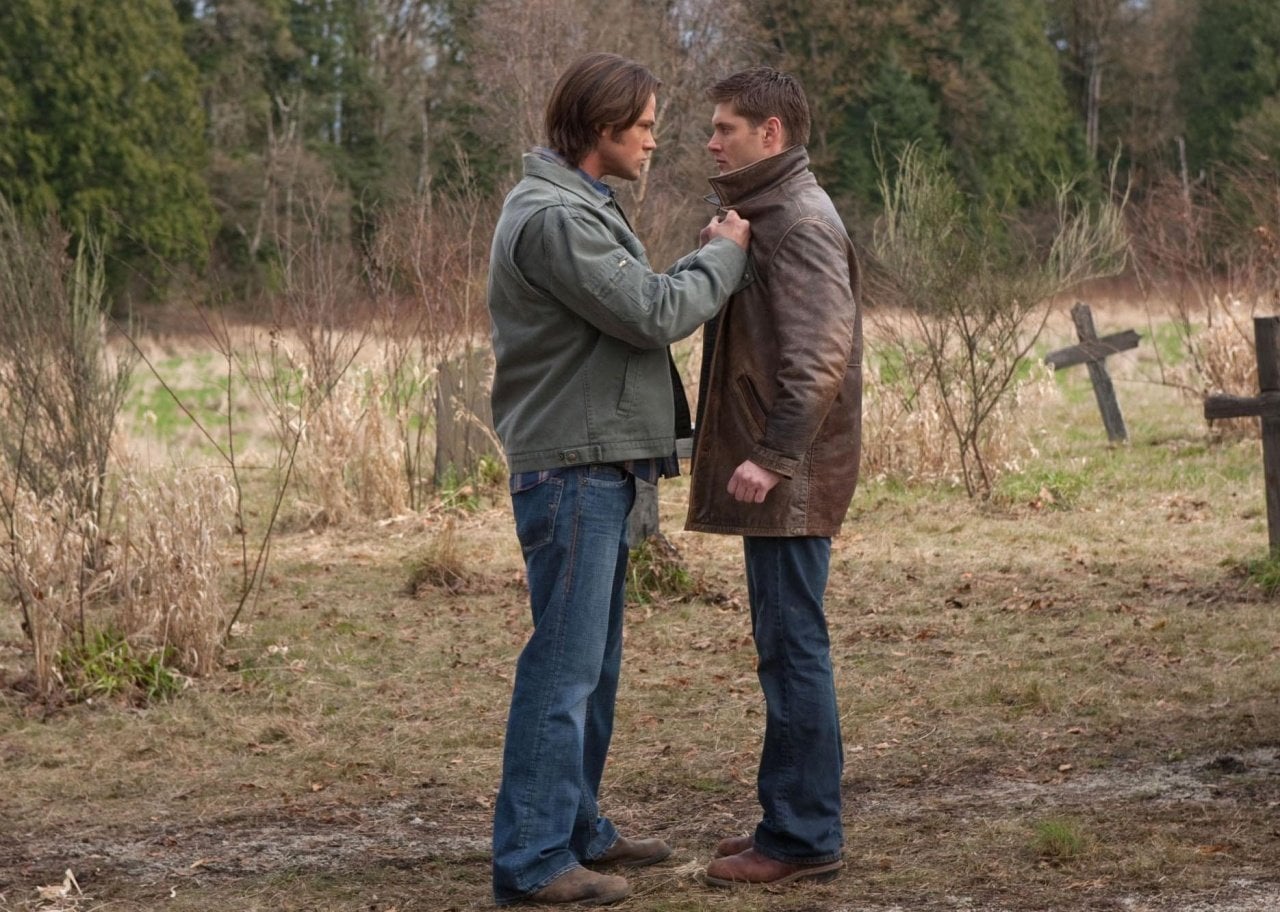 Two men stand next to crosses in the ground, one grabbing the other by the collar.