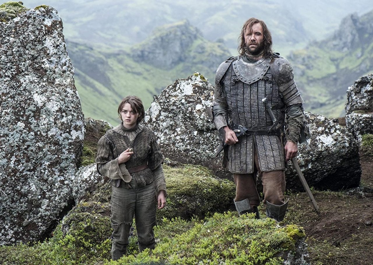 A little girl and a man wearing armor stand in the mountains.