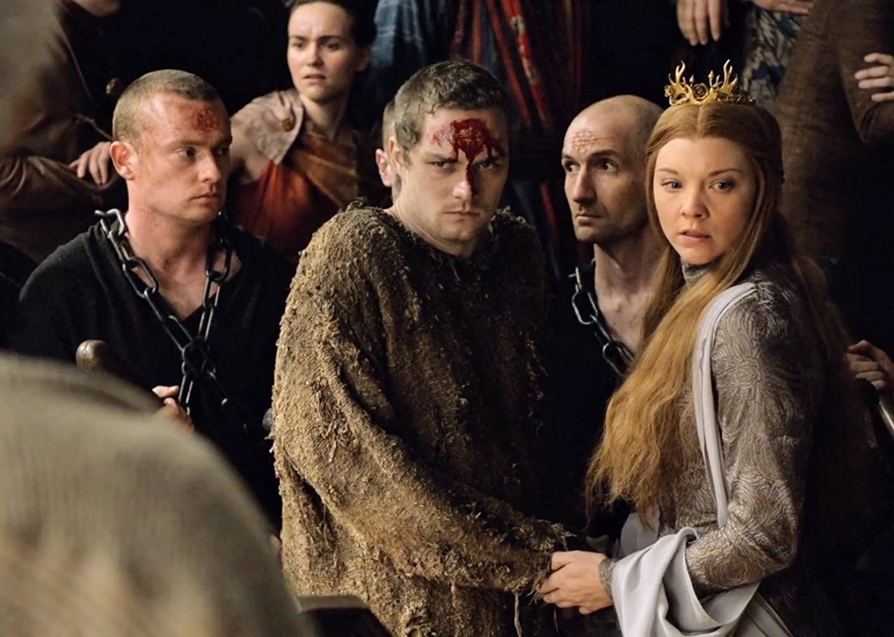 A woman in a crown stands next to a man with blood on his forehead in a crowd.