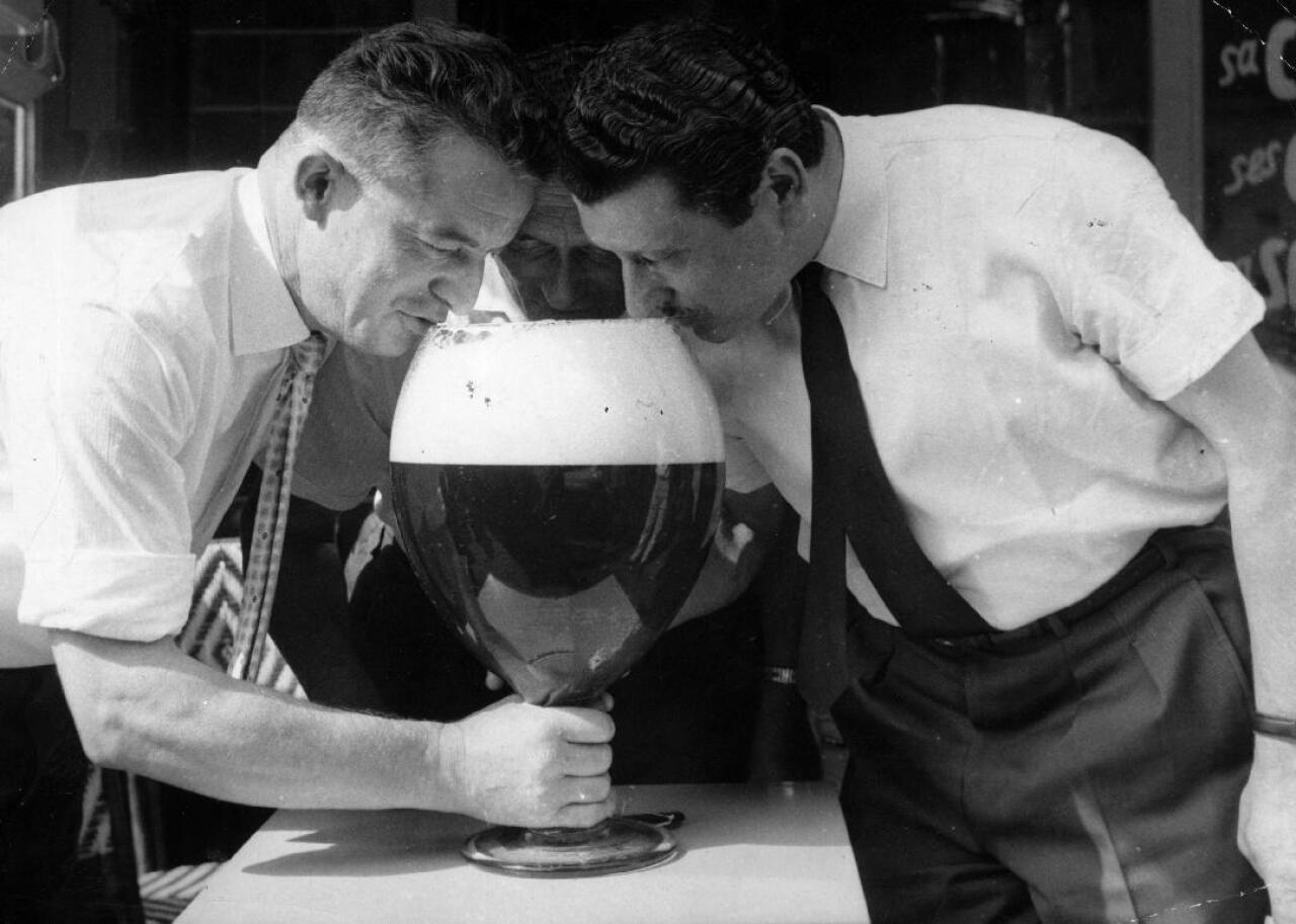 Two men take a sip from a large beer glass.