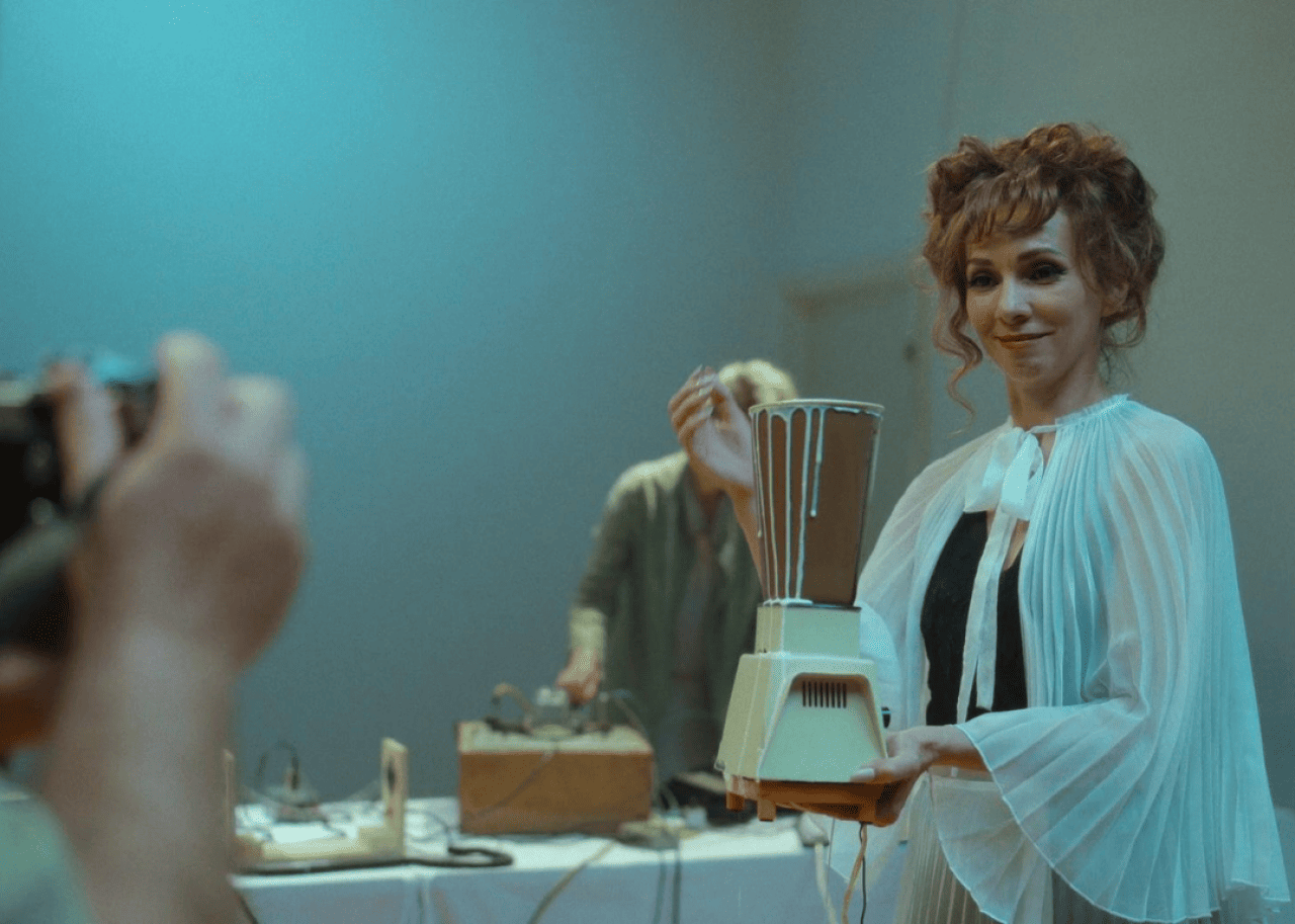 A woman smiling while holding an overfilled blender.