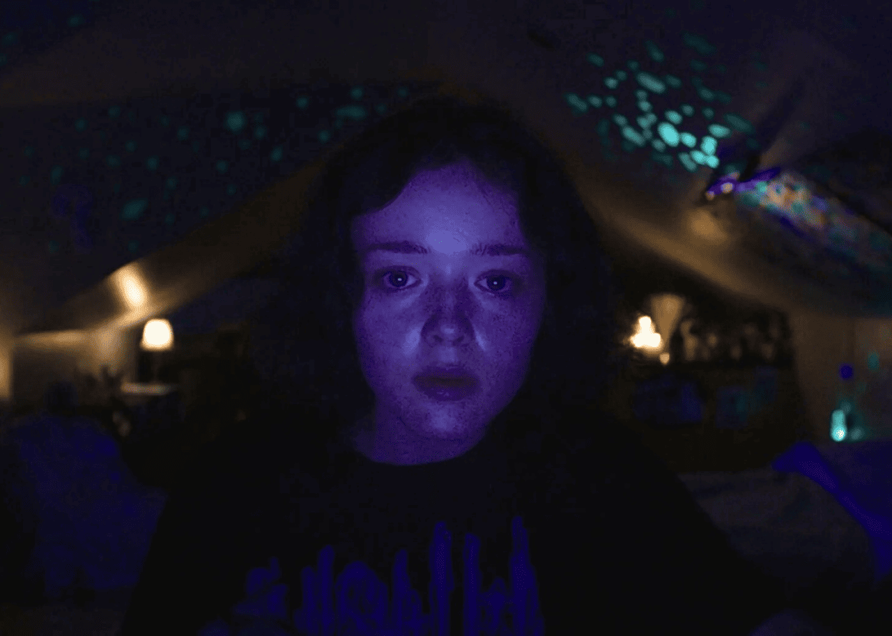 A girl in a dark room with computer screen lighting up her face.